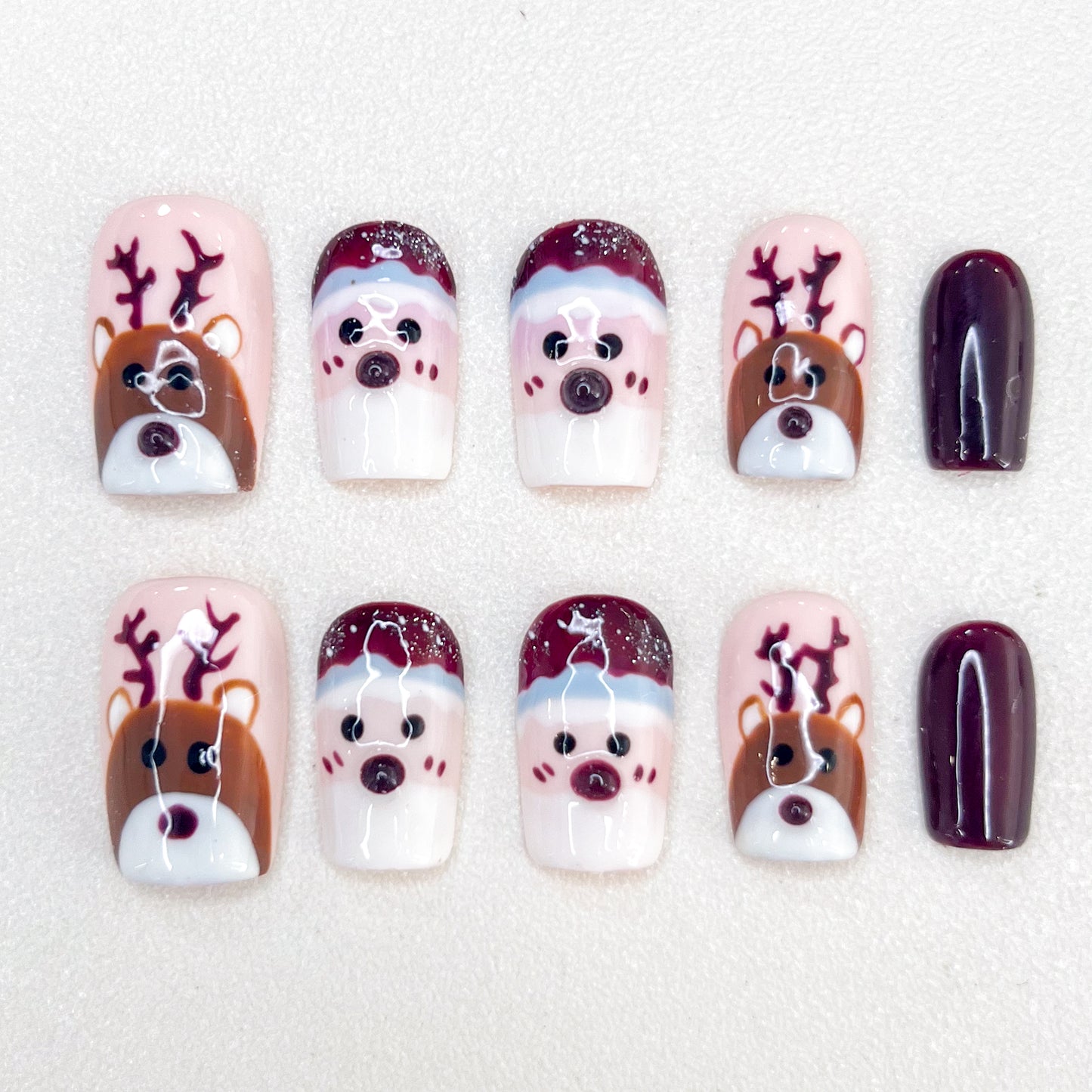 Festive Christmas press-on nails with charming reindeer and Santa faces, accented by deep burgundy tones.