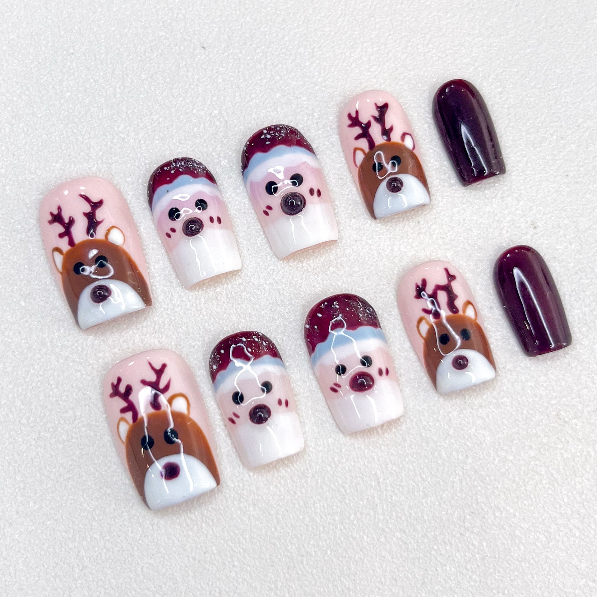 Festive Christmas press-on nails with charming reindeer and Santa faces, accented by deep burgundy tones.