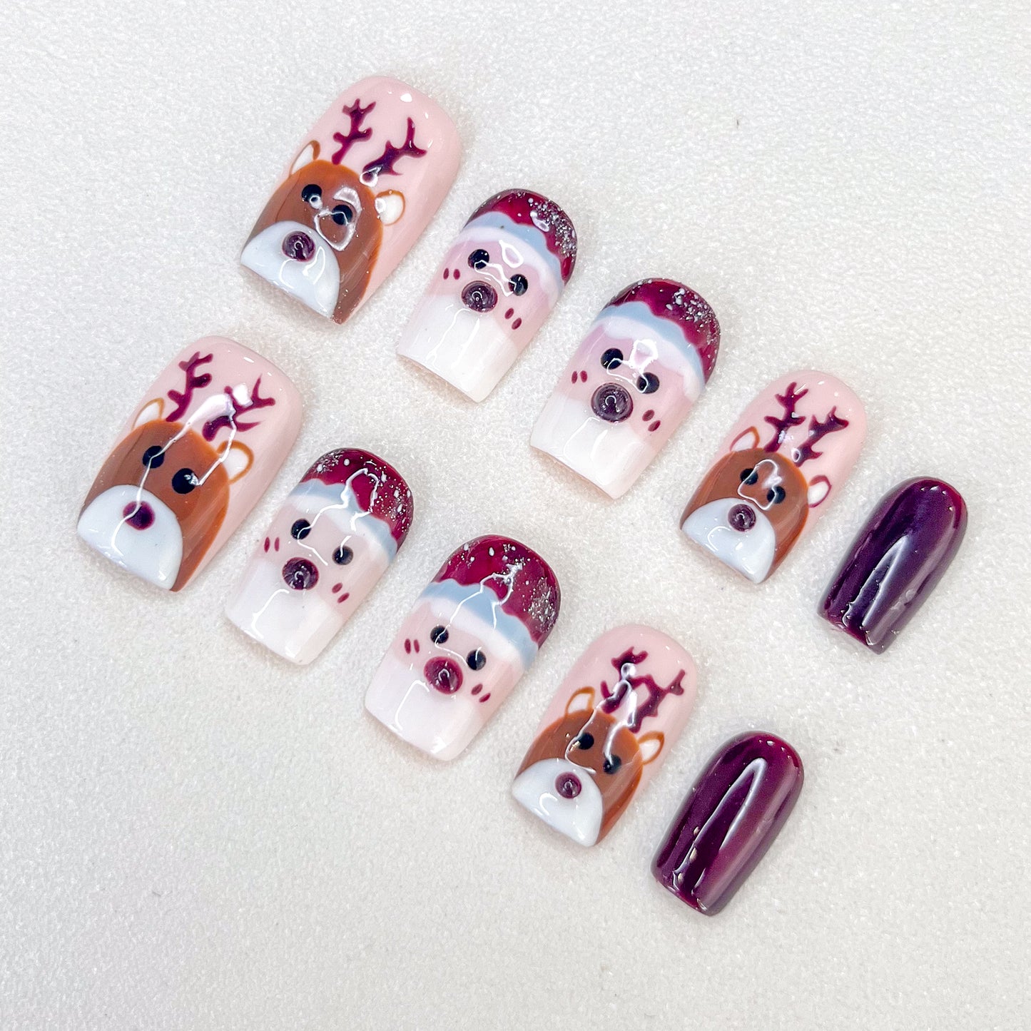 Festive Christmas press-on nails with charming reindeer and Santa faces, accented by deep burgundy tones.