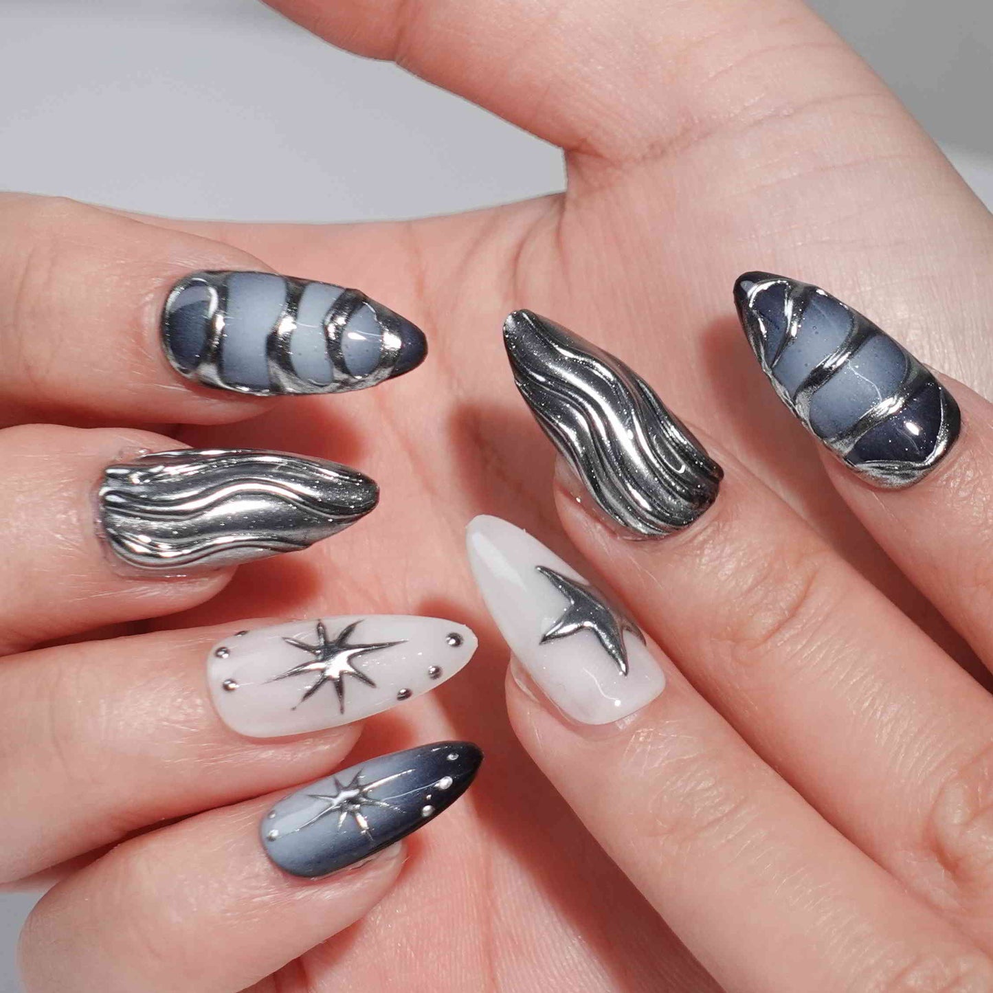 A set of press - on nails with dark blue and silver wave patterns like cosmic designs, and star - shaped accents. The nails have a celestial and stylish appearance, suitable for parties or futuristic - themed events.