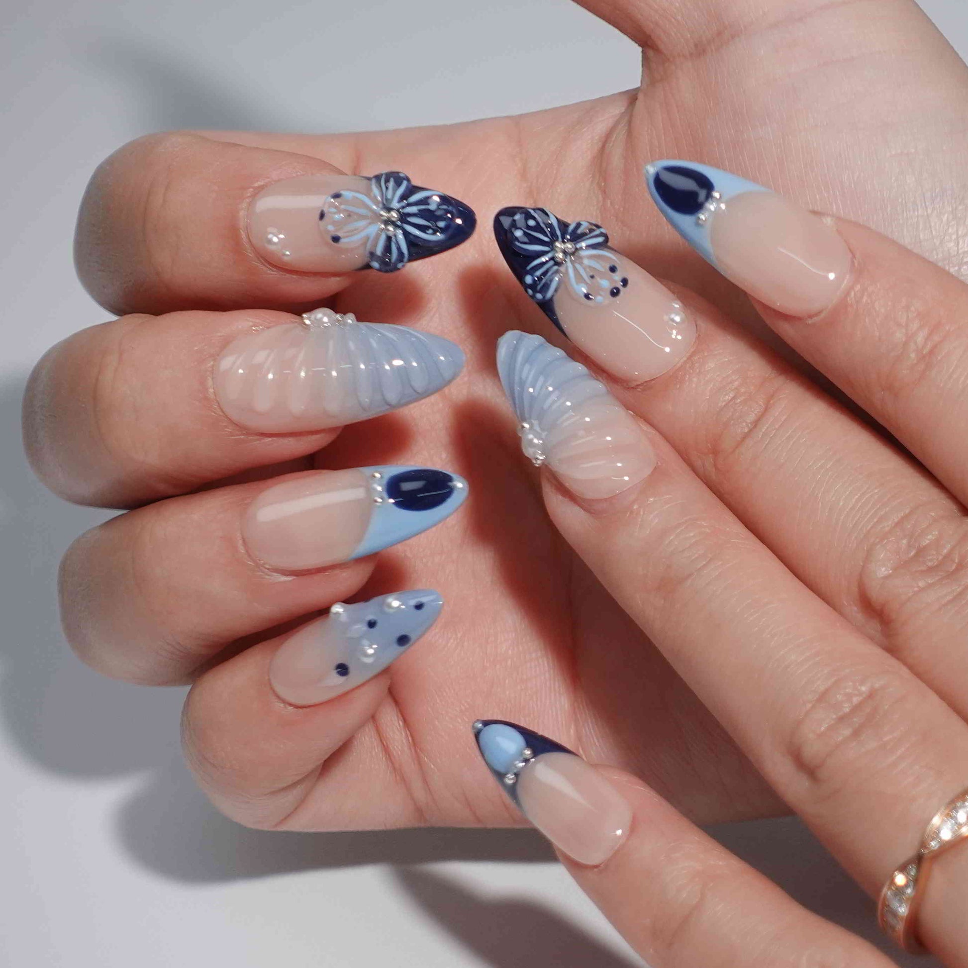 A mesmerizing set of handmade press-on nails with pink and navy hues, adorned with shimmering pearls, sculpted seashell elements, and elegant bows, evoking the tranquil beauty of moonlit ocean waves.