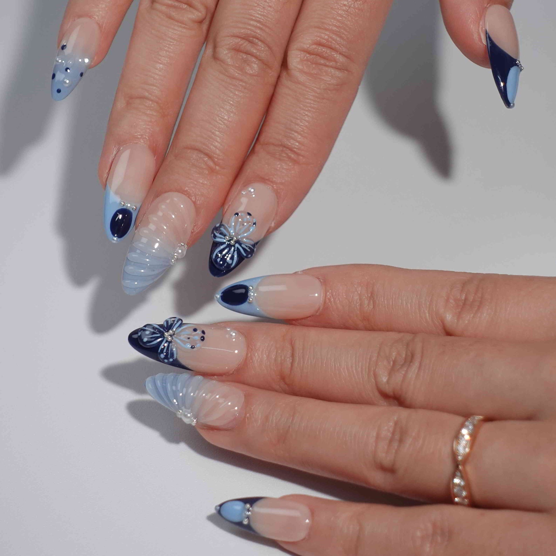 A mesmerizing set of handmade press-on nails with pink and navy hues, adorned with shimmering pearls, sculpted seashell elements, and elegant bows, evoking the tranquil beauty of moonlit ocean waves.