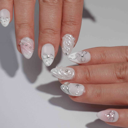 A set of press-on nails featuring pastel pink and white tones adorned with silver bows, pearls, and shimmering accents. The design exudes elegance and sophistication, ideal for formal or festive occasions.