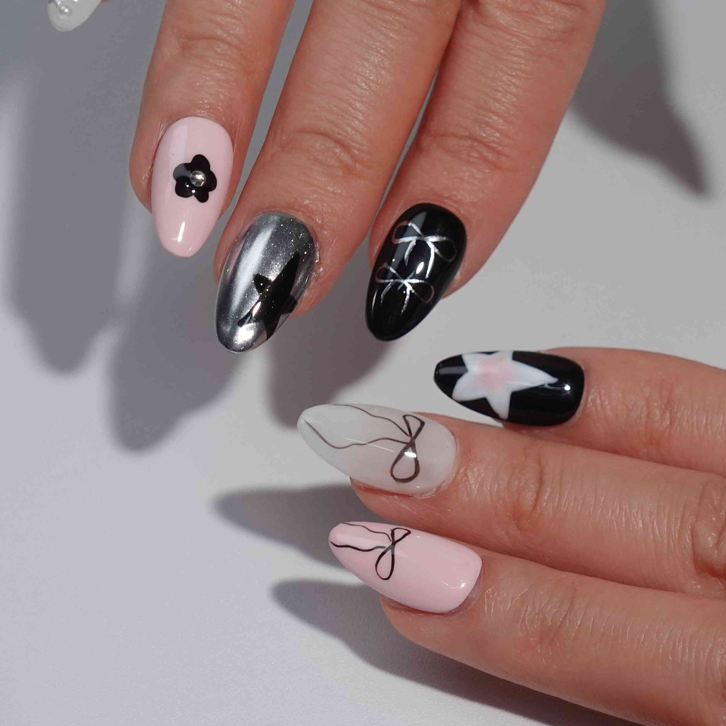 A set of press - on nails with a glamorous mix of pink and black colors, featuring stylish designs such as bows, stars, and flowers. The nails have a chic and fashionable appearance, suitable for both casual and formal events.