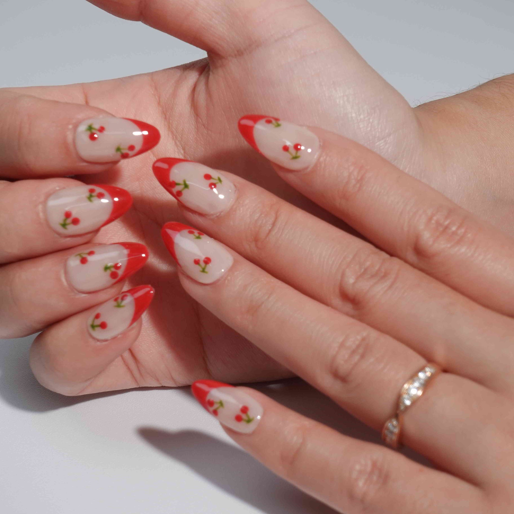 A cheerful nail design named "Cherry Delight," featuring nude nails with crisp white French tips, accented by tiny red cherries with green stems. This set captures the essence of a sunlit cherry orchard, bringing a splash of fresh energy to any look.