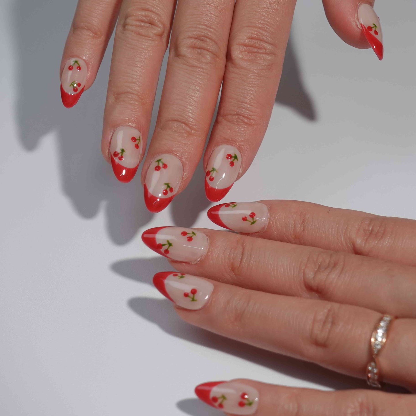 A cheerful nail design named "Cherry Delight," featuring nude nails with crisp white French tips, accented by tiny red cherries with green stems. This set captures the essence of a sunlit cherry orchard, bringing a splash of fresh energy to any look.