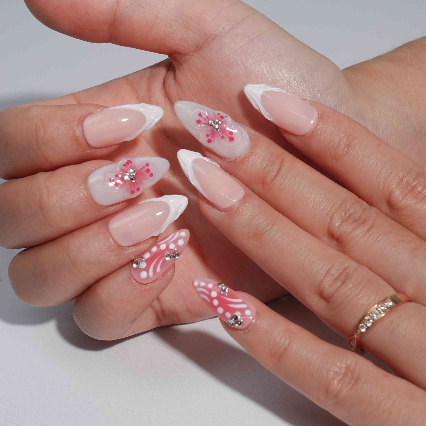 A handmade set of press-on nails showcasing pink gradients, intricate white petal-like designs, and 3D floral centers adorned with rhinestones, evoking the charm of blooming spring flowers under soft sunlight.