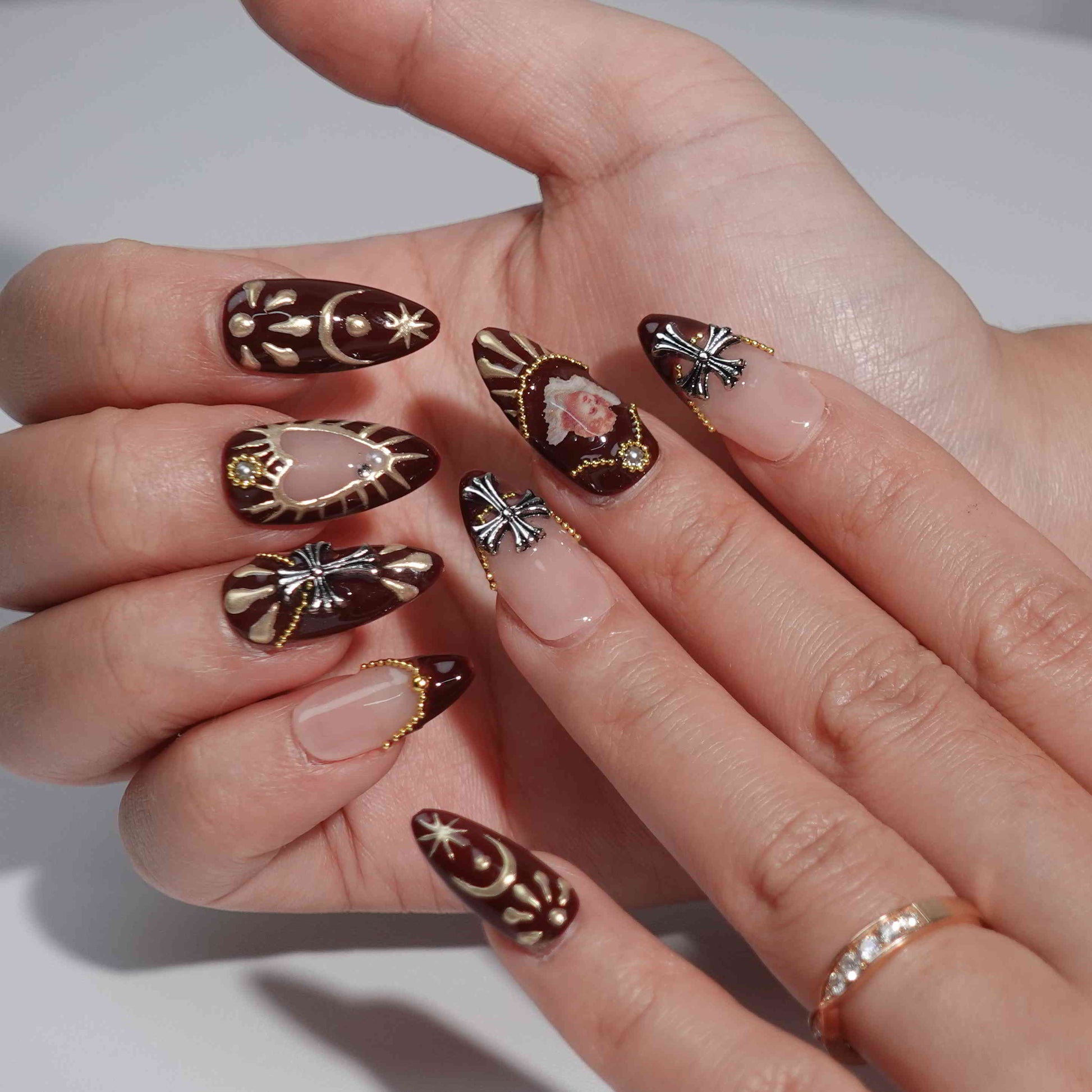 A luxurious set of burgundy press-on nails with golden details, pearl ornaments, hand-painted cherub motifs, and gothic-style crosses, evoking the grandeur and elegance of the Baroque era. Ideal for statement looks.