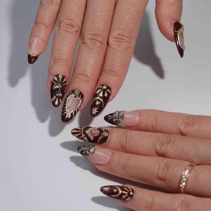 A luxurious set of burgundy press-on nails with golden details, pearl ornaments, hand-painted cherub motifs, and gothic-style crosses, evoking the grandeur and elegance of the Baroque era. Ideal for statement looks.