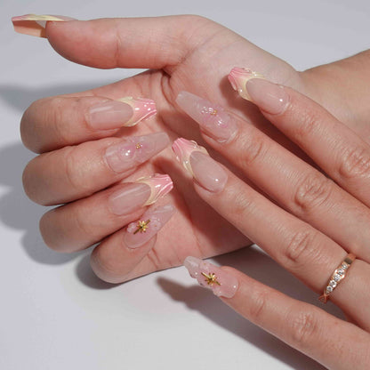 A stunning set of handmade press-on nails with soft pink gradients, beautifully sculpted petal edges, 3D flowers, and golden star decorations, evoking an elegant and dreamy aesthetic.