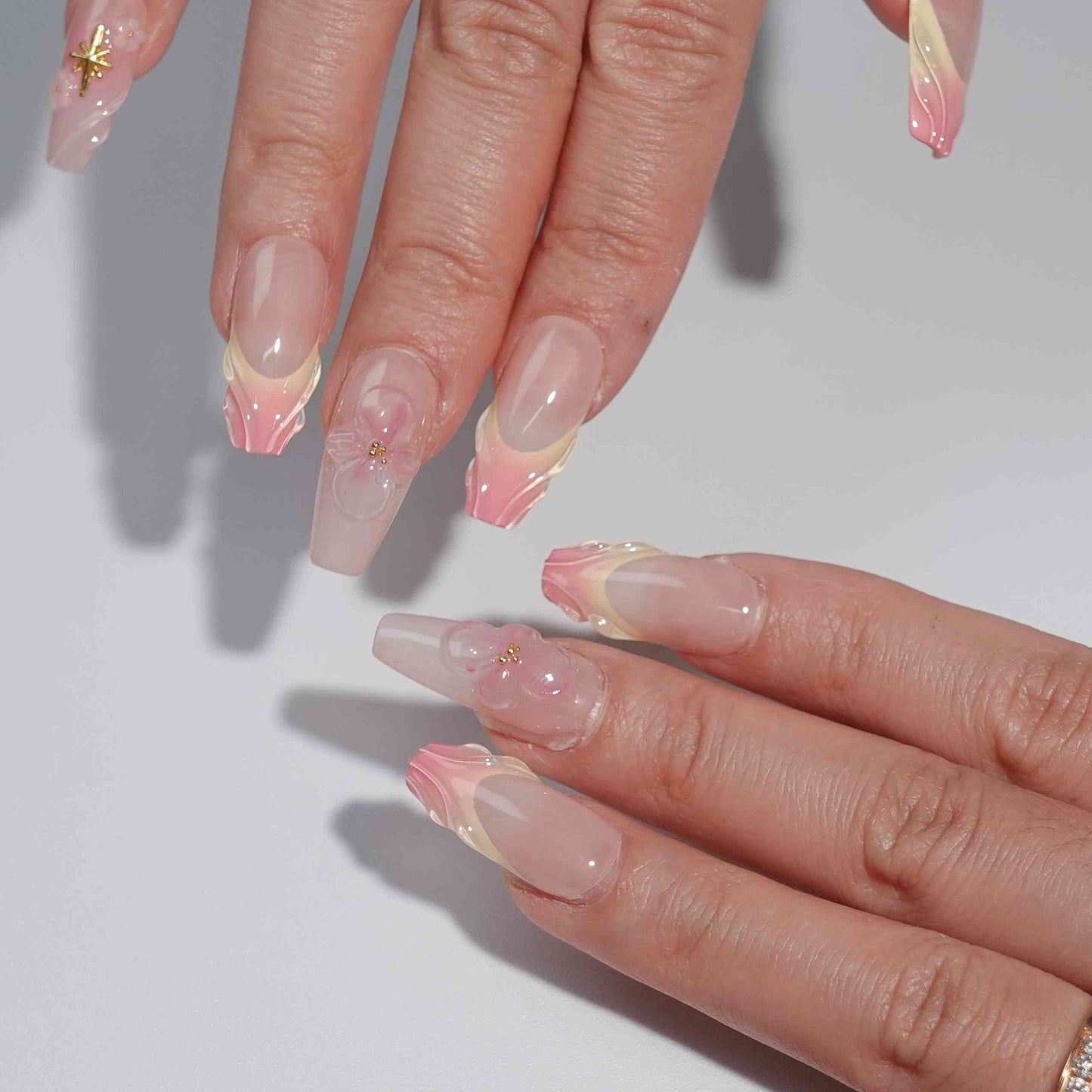 A stunning set of handmade press-on nails with soft pink gradients, beautifully sculpted petal edges, 3D flowers, and golden star decorations, evoking an elegant and dreamy aesthetic.