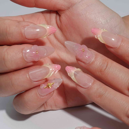 A handmade set of press-on nails showcasing pink and peach ombré designs with sculpted petal-like tips, complemented by 3D floral accents and golden embellishments, exuding elegance and delicate charm.