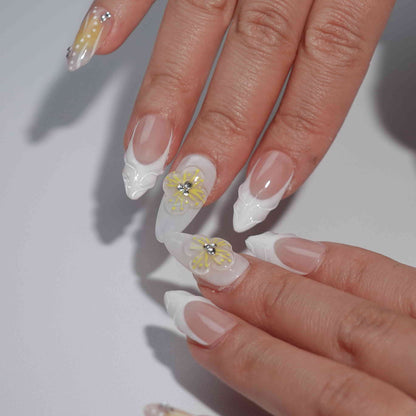 A bright and cheerful handmade set of press-on nails featuring soft yellow-to-peach gradients, 3D floral embellishments, and sparkling rhinestone details, evoking the warmth and light of a summer sunrise.