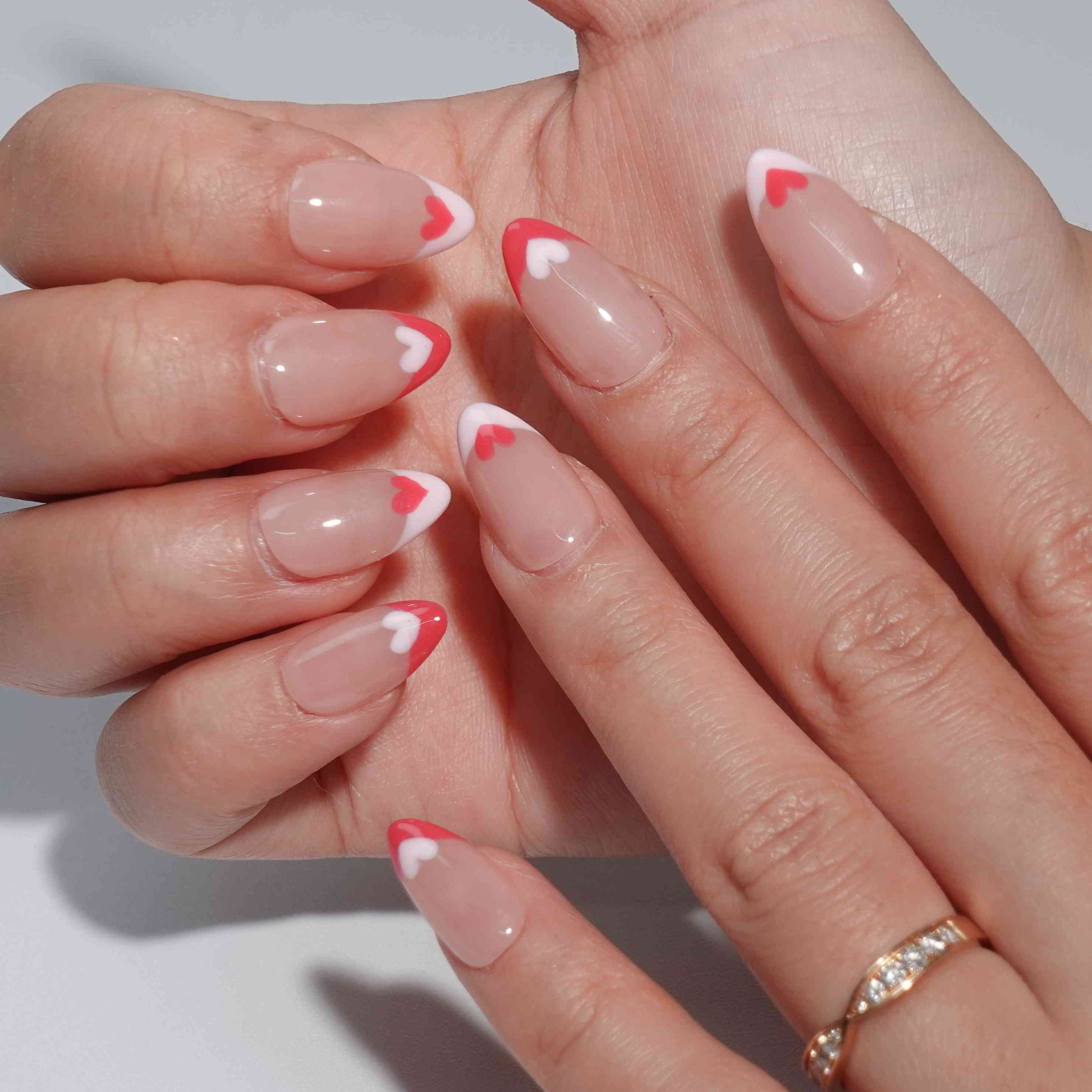 Nude nails with bold red French tips, each adorned with alternating red and white heart accents. This heartfelt design exudes romance and timeless elegance, perfect for adding a touch of love to your style.