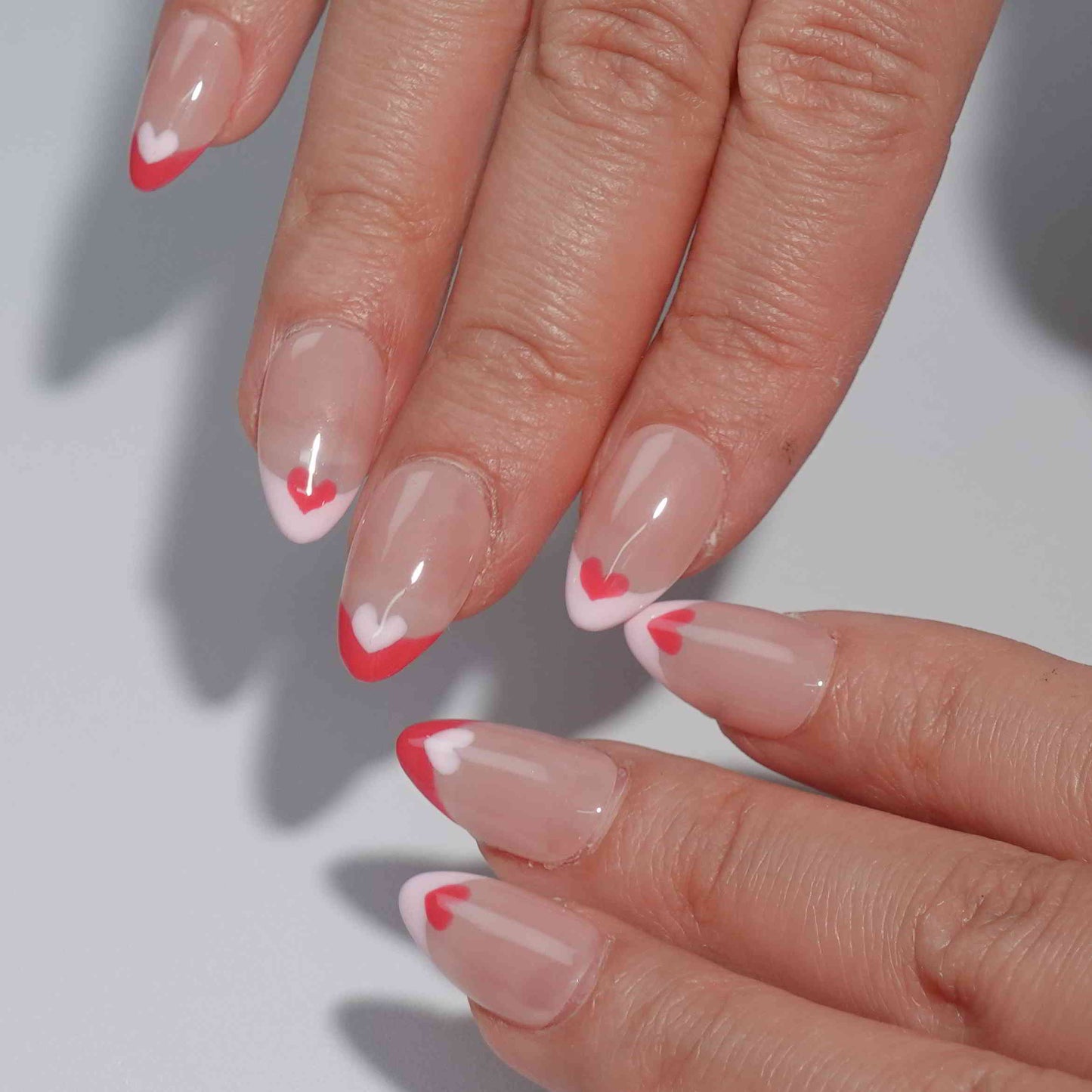 Nude nails with bold red French tips, each adorned with alternating red and white heart accents. This heartfelt design exudes romance and timeless elegance, perfect for adding a touch of love to your style.