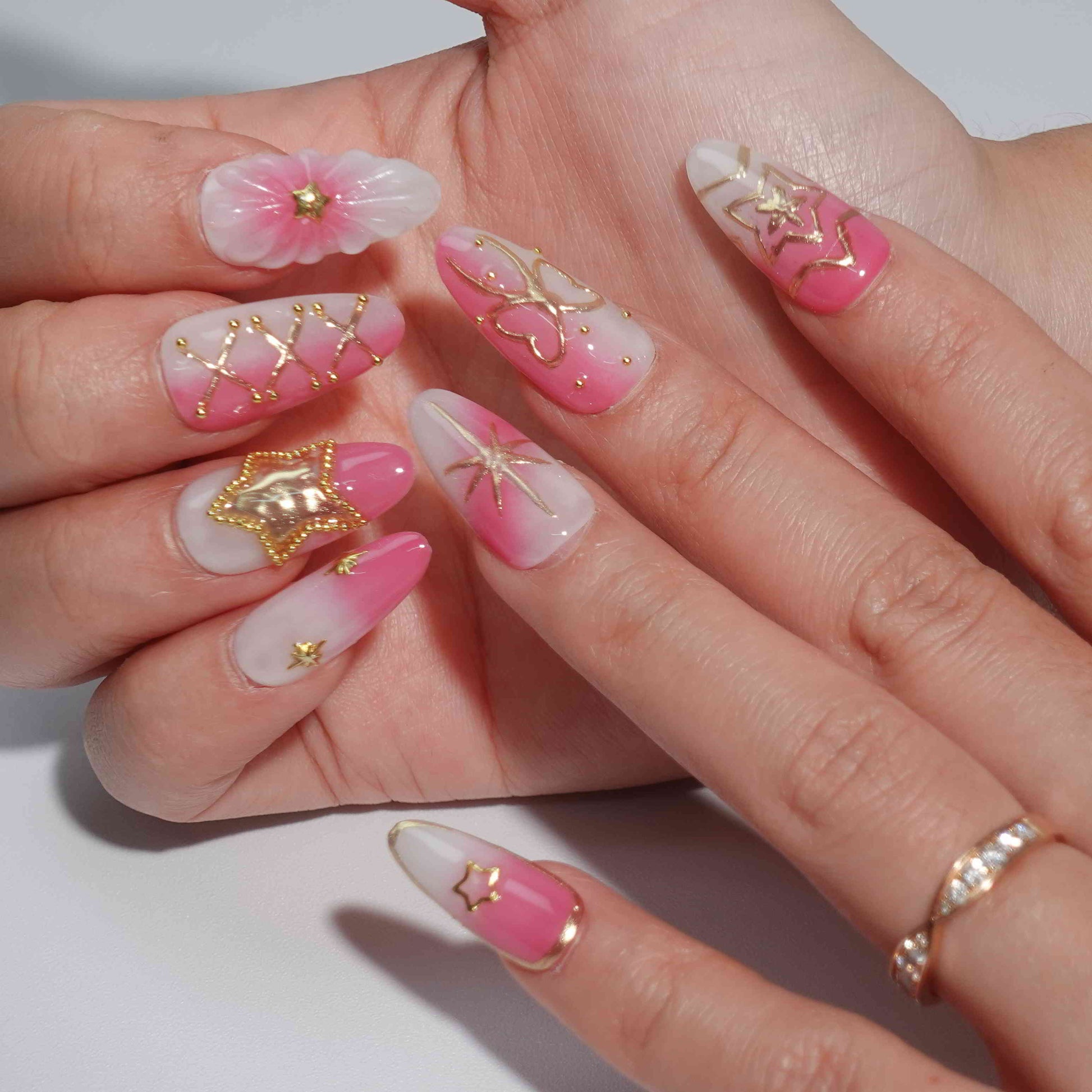 A stunning set of handmade press-on nails featuring celestial-themed designs, including golden stars, moons, and bows, with a graceful pink and white gradient.