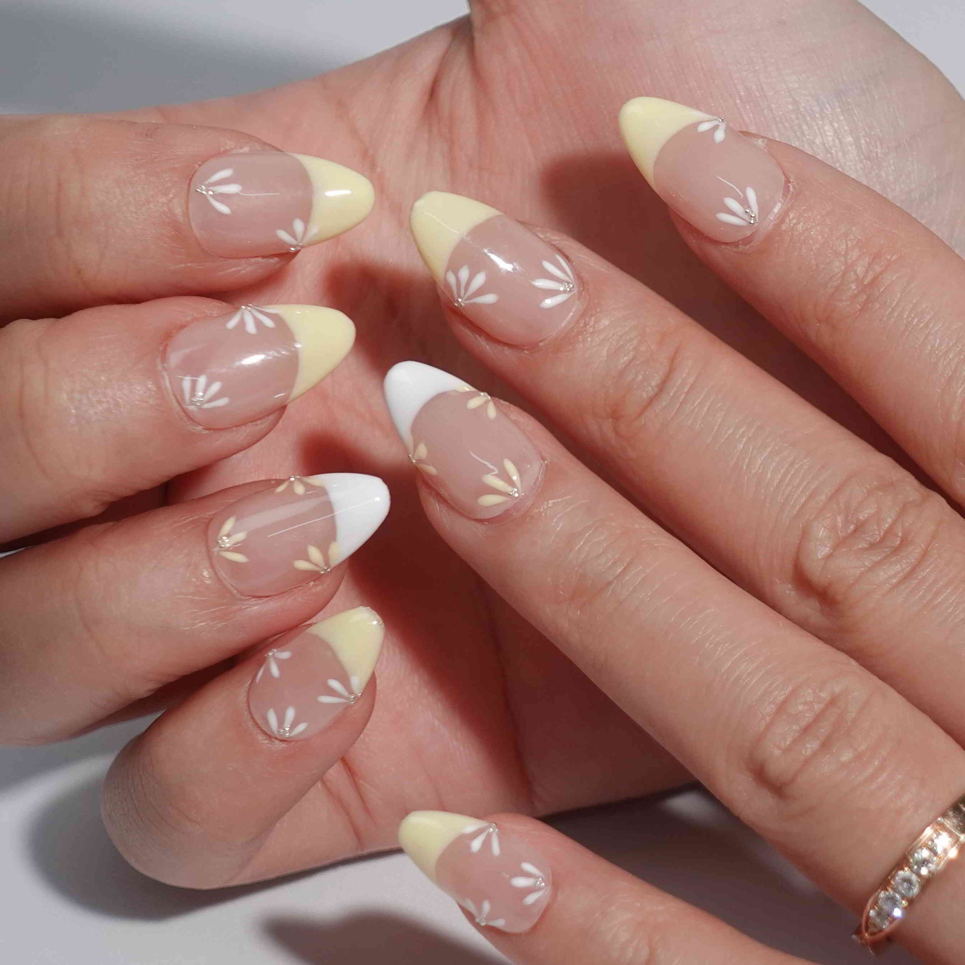 Nude nails with yellow and white French tips, enhanced by delicate daisy-inspired floral accents. Each flower alternates between yellow and white petals with a shimmering diamond at the center, evoking the tranquil beauty of a sunlit meadow.