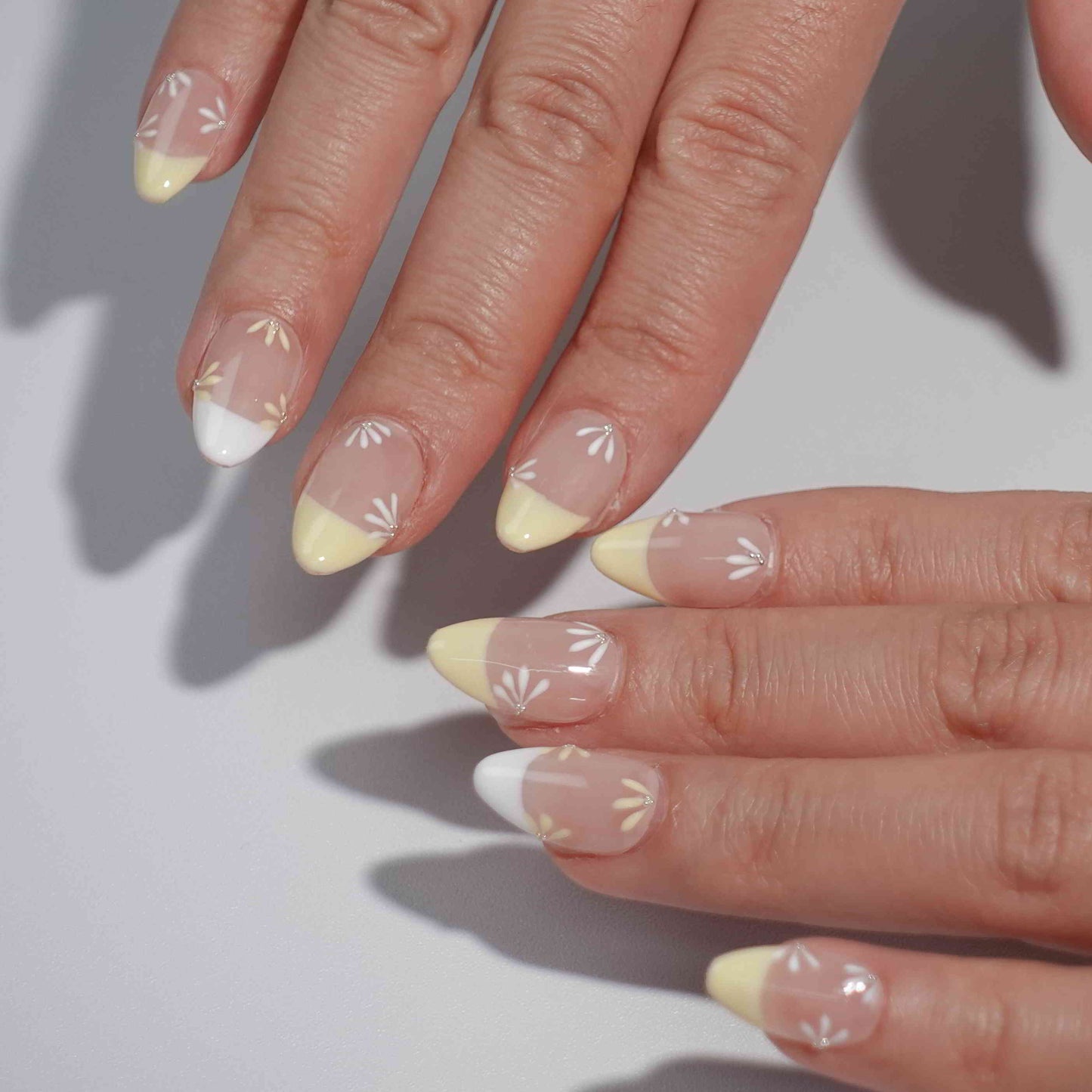 Nude nails with yellow and white French tips, enhanced by delicate daisy-inspired floral accents. Each flower alternates between yellow and white petals with a shimmering diamond at the center, evoking the tranquil beauty of a sunlit meadow.