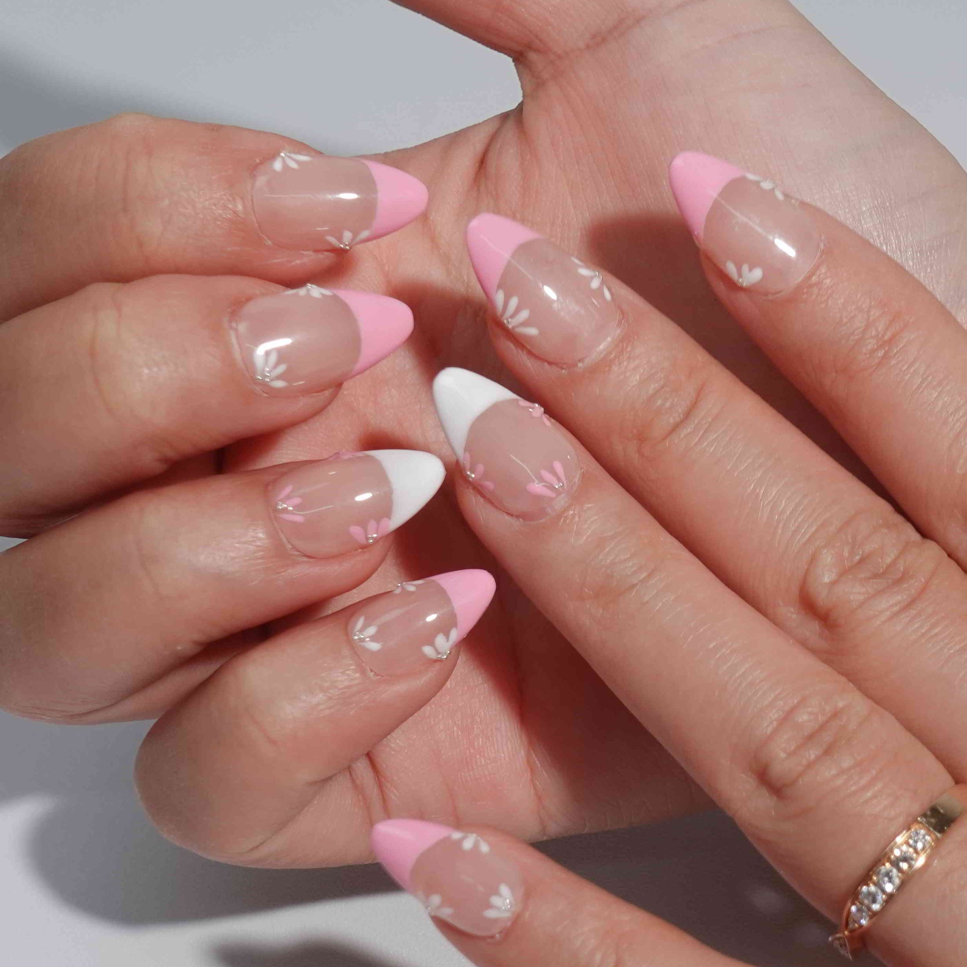 A feminine nail design named "Blush Petals," showcasing pink and white French tips with soft floral accents in matching hues. Each flower is delicately painted with a shimmering rhinestone center, evoking the romance of spring gardens in full bloom.