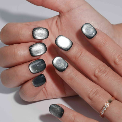 A set of gunmetal - colored glossy press - on nails worn on a person's hand. The nails have a smooth, shiny finish with a metallic appearance, giving them a bold and stylish look. The gunmetal hue adds an edgy flair, suitable for party or nightlife settings.