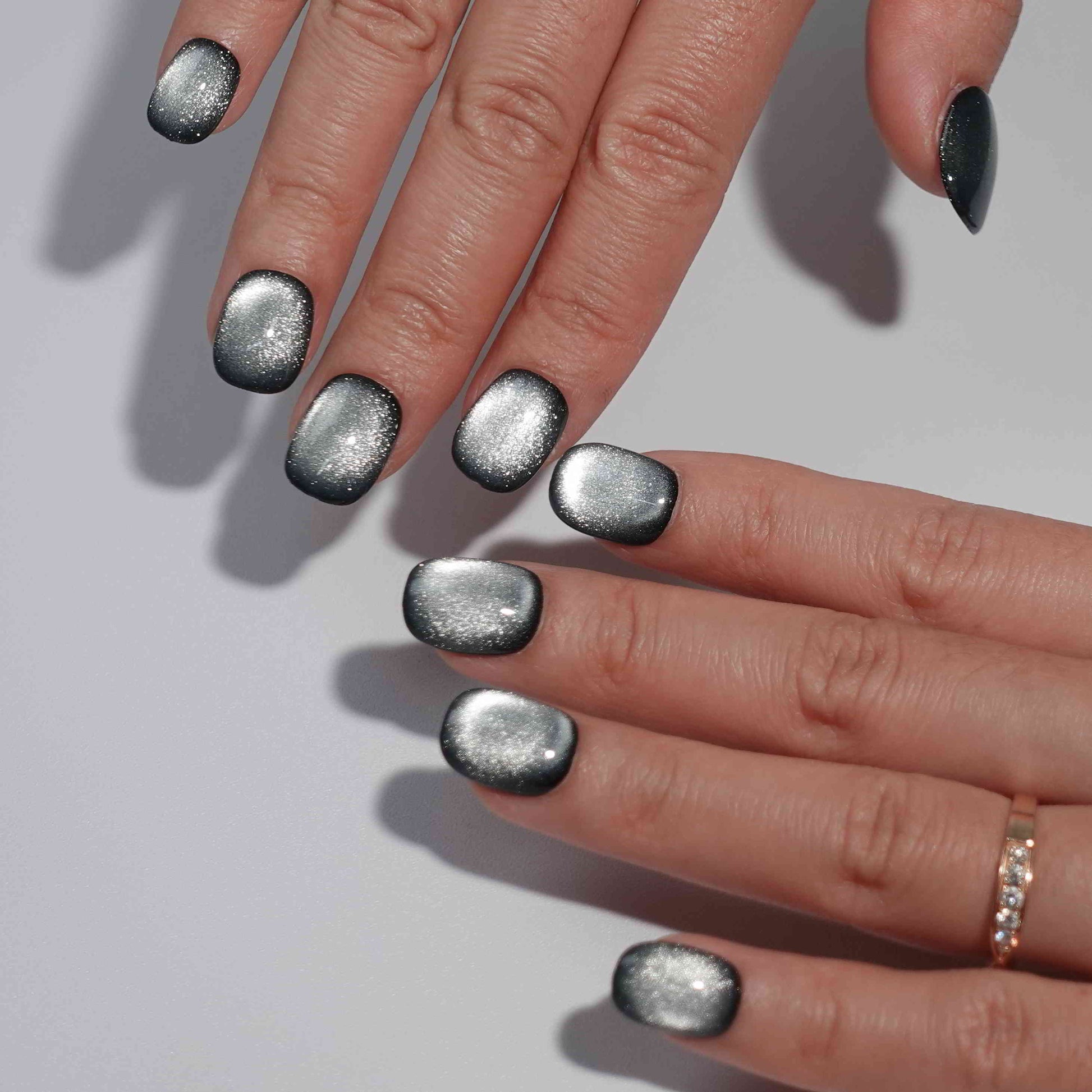 A set of gunmetal - colored glossy press - on nails worn on a person's hand. The nails have a smooth, shiny finish with a metallic appearance, giving them a bold and stylish look. The gunmetal hue adds an edgy flair, suitable for party or nightlife settings.