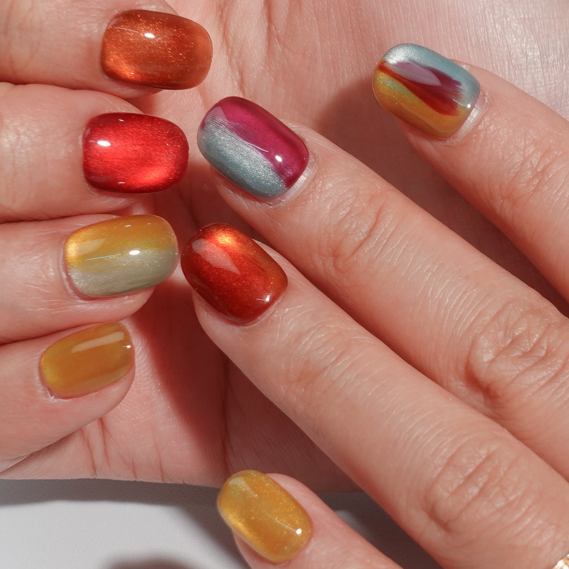 A set of press - on nails with a captivating mix of colors resembling the aurora borealis, neatly arranged in a transparent case. The nails have an iridescent, dreamy finish, ideal for making a statement at parties or creative events.