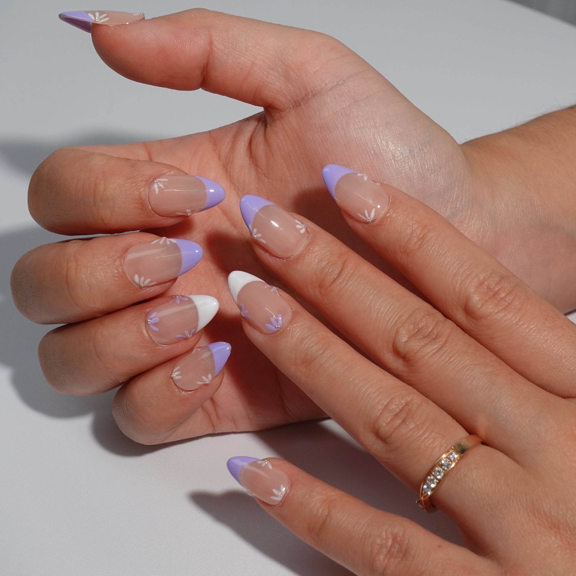 Press-on nails with a nude base, purple and white French tip design, accented with intricate floral details for a refined and spring-inspired look.