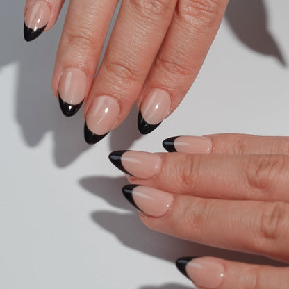 A bold nail design named "Eclipse Noir," combining nude nails with sleek black French tips. This set evokes the mystique and contrast of a lunar eclipse, offering a contemporary take on timeless elegance for evenings or formal occasions.