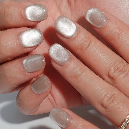 A set of silver glossy press - on nails worn on a person's hand, showcasing a smooth and shiny finish. The nails have an elegant oval shape, complementing the natural contours of the fingers. The silver color adds a touch of class, making it suitable for formal or evening wear.