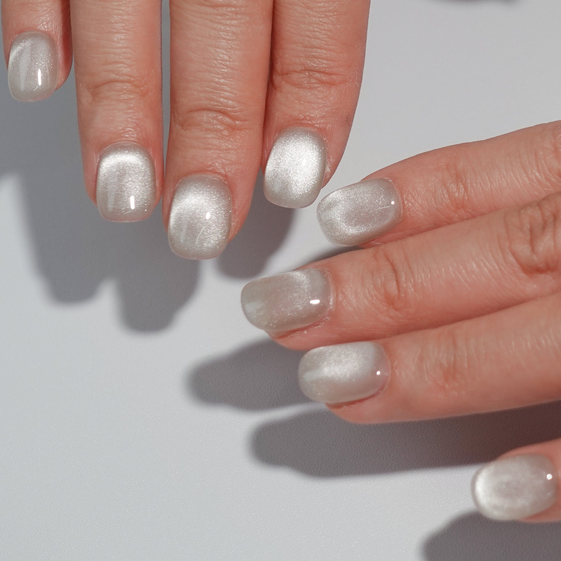 A set of silver glossy press - on nails worn on a person's hand, showcasing a smooth and shiny finish. The nails have an elegant oval shape, complementing the natural contours of the fingers. The silver color adds a touch of class, making it suitable for formal or evening wear.