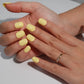 A set of bright yellow glossy press-on nails neatly arranged in a transparent case, featuring a vibrant and smooth finish, ideal for everyday wear, with a warm and natural backdrop.