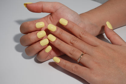 A set of bright yellow glossy press-on nails neatly arranged in a transparent case, featuring a vibrant and smooth finish, ideal for everyday wear, with a warm and natural backdrop.