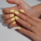 A set of bright yellow glossy press-on nails neatly arranged in a transparent case, featuring a vibrant and smooth finish, ideal for everyday wear, with a warm and natural backdrop.
