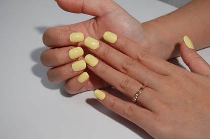 A set of bright yellow glossy press-on nails neatly arranged in a transparent case, featuring a vibrant and smooth finish, ideal for everyday wear, with a warm and natural backdrop.