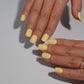 A set of bright yellow glossy press-on nails neatly arranged in a transparent case, featuring a vibrant and smooth finish, ideal for everyday wear, with a warm and natural backdrop.