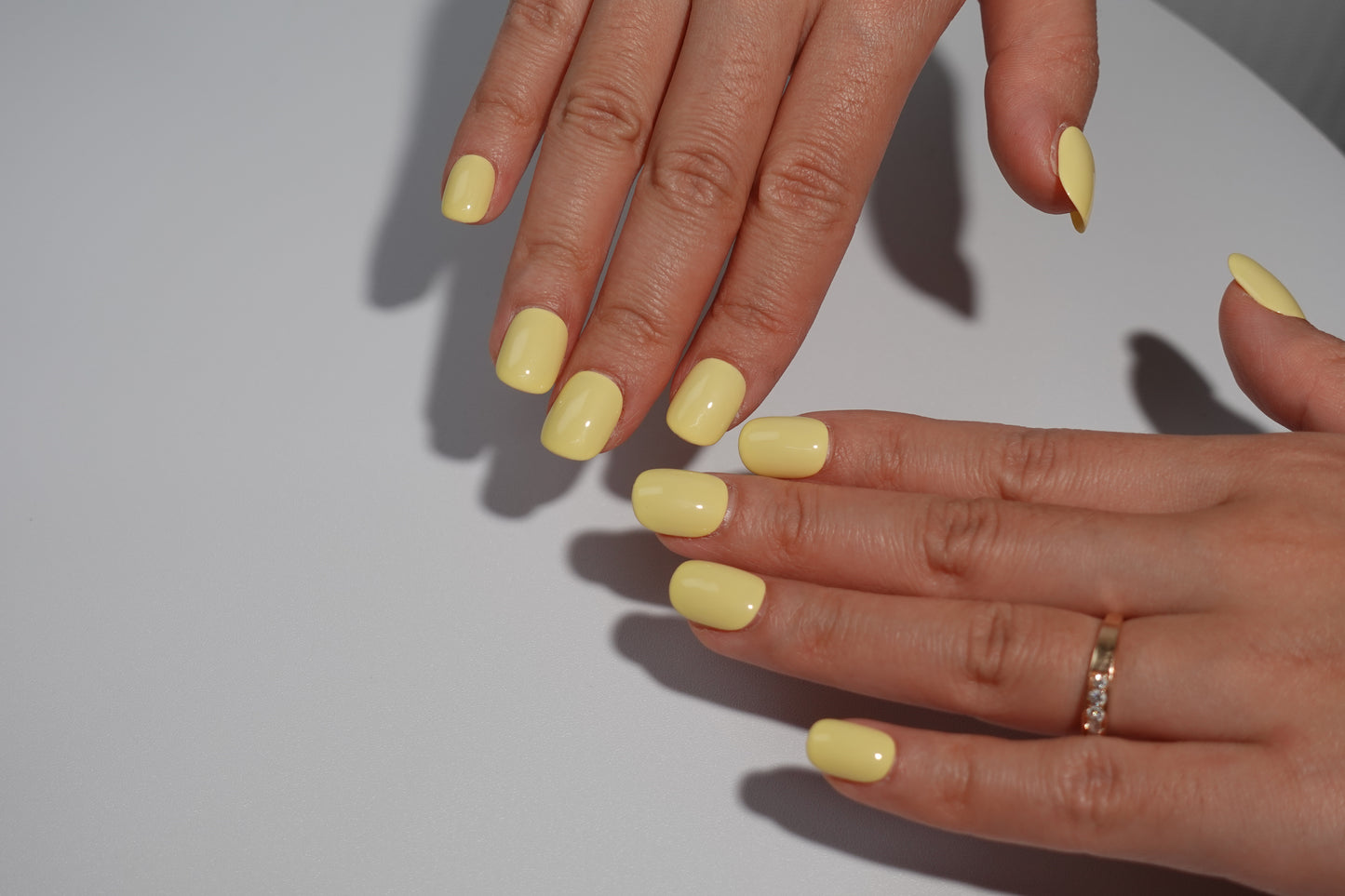 A set of bright yellow glossy press-on nails neatly arranged in a transparent case, featuring a vibrant and smooth finish, ideal for everyday wear, with a warm and natural backdrop.