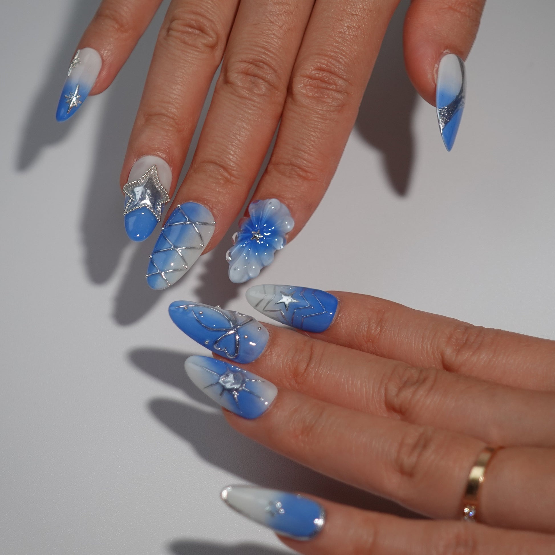  A celestial-themed press-on nail set showcasing silver star embellishments, intricate bows, and a soft blue-to-white gradient. The design evokes the tranquility and wonder of a star-filled night sky.