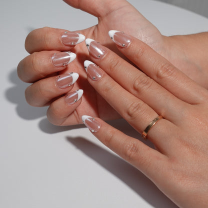 Nude nails adorned with dazzling white French tips and embellished with sparkling diamond accents. The design exudes an ethereal charm, reminiscent of moonlight reflecting on a serene lake.