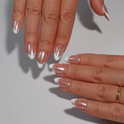 Nude nails adorned with dazzling white French tips and embellished with sparkling diamond accents. The design exudes an ethereal charm, reminiscent of moonlight reflecting on a serene lake.