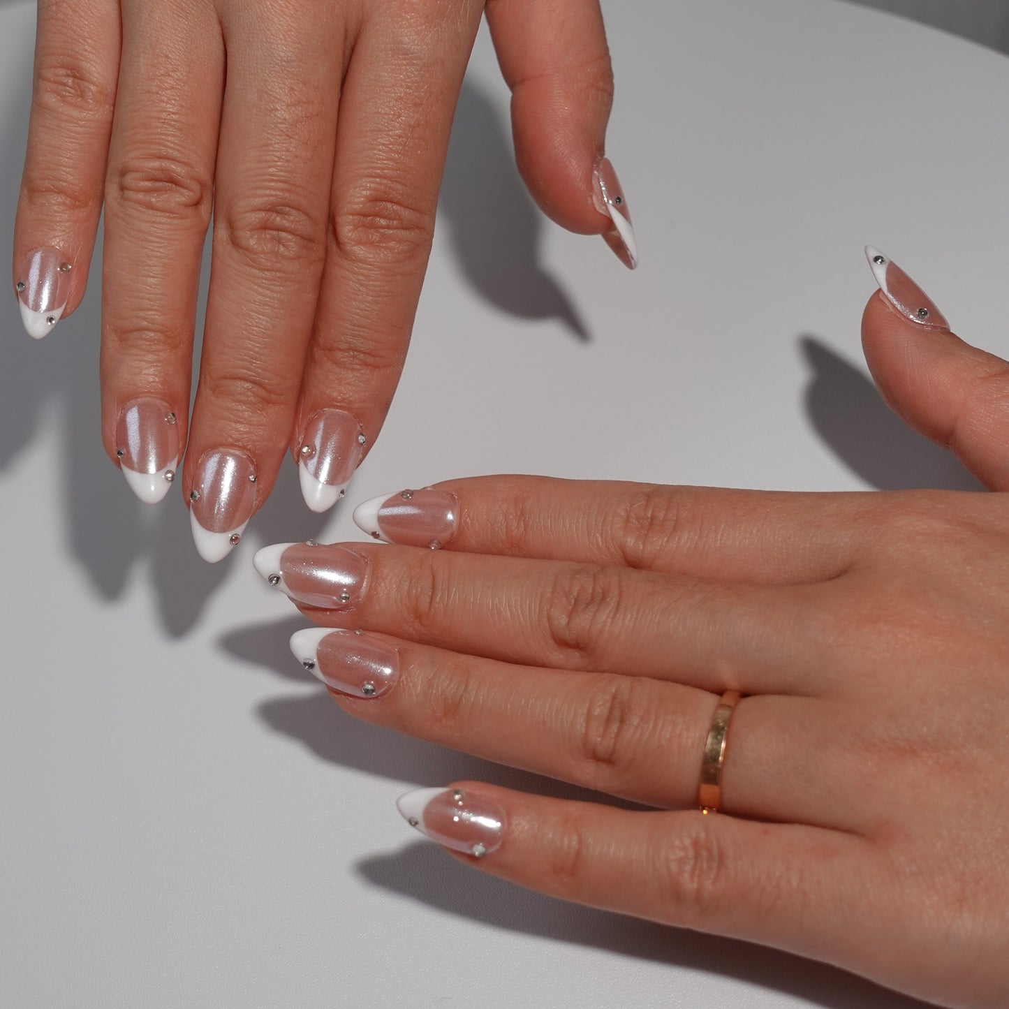 Nude nails adorned with dazzling white French tips and embellished with sparkling diamond accents. The design exudes an ethereal charm, reminiscent of moonlight reflecting on a serene lake.