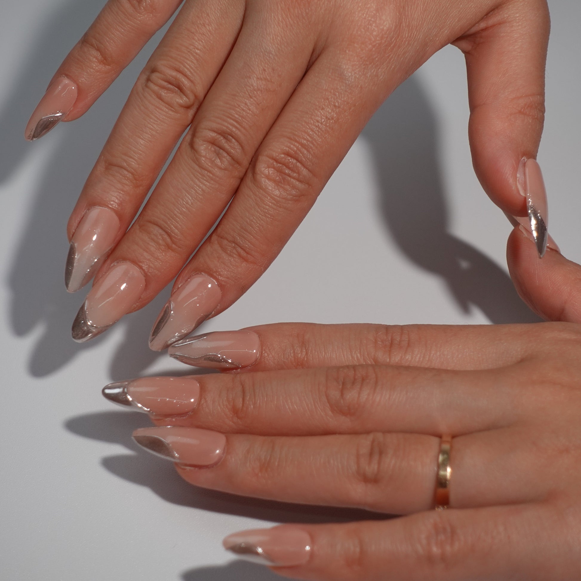 A set of chic nude nails adorned with flowing silver metallic patterns. The shimmering accents create a contemporary design that captures the essence of urban elegance and high fashion.