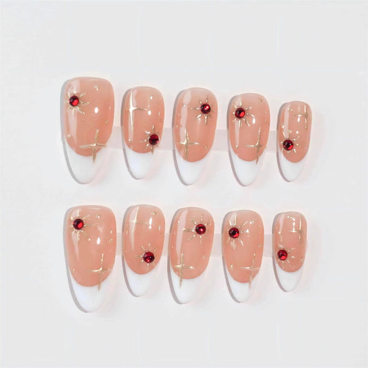 Press-on nails with a nude base, white French tips, decorated with gold star patterns and striking red gem embellishments, creating an elegant and festive design.