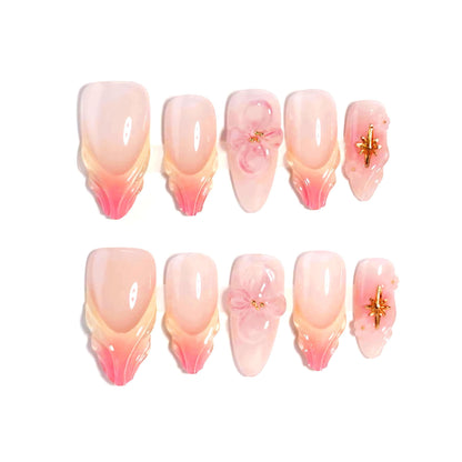 A handmade set of press-on nails showcasing pink and peach ombré designs with sculpted petal-like tips, complemented by 3D floral accents and golden embellishments, exuding elegance and delicate charm.