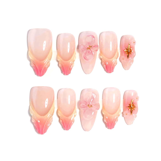 A handmade set of press-on nails showcasing pink and peach ombré designs with sculpted petal-like tips, complemented by 3D floral accents and golden embellishments, exuding elegance and delicate charm.