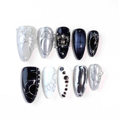 A luxurious set of press-on nails combining glossy black, crisp white, and shimmering silver tones. Featuring textures like metallic chrome, abstract patterns, and a fleur-de-lis embellishment, these nails are designed for bold, high-fashion statements.