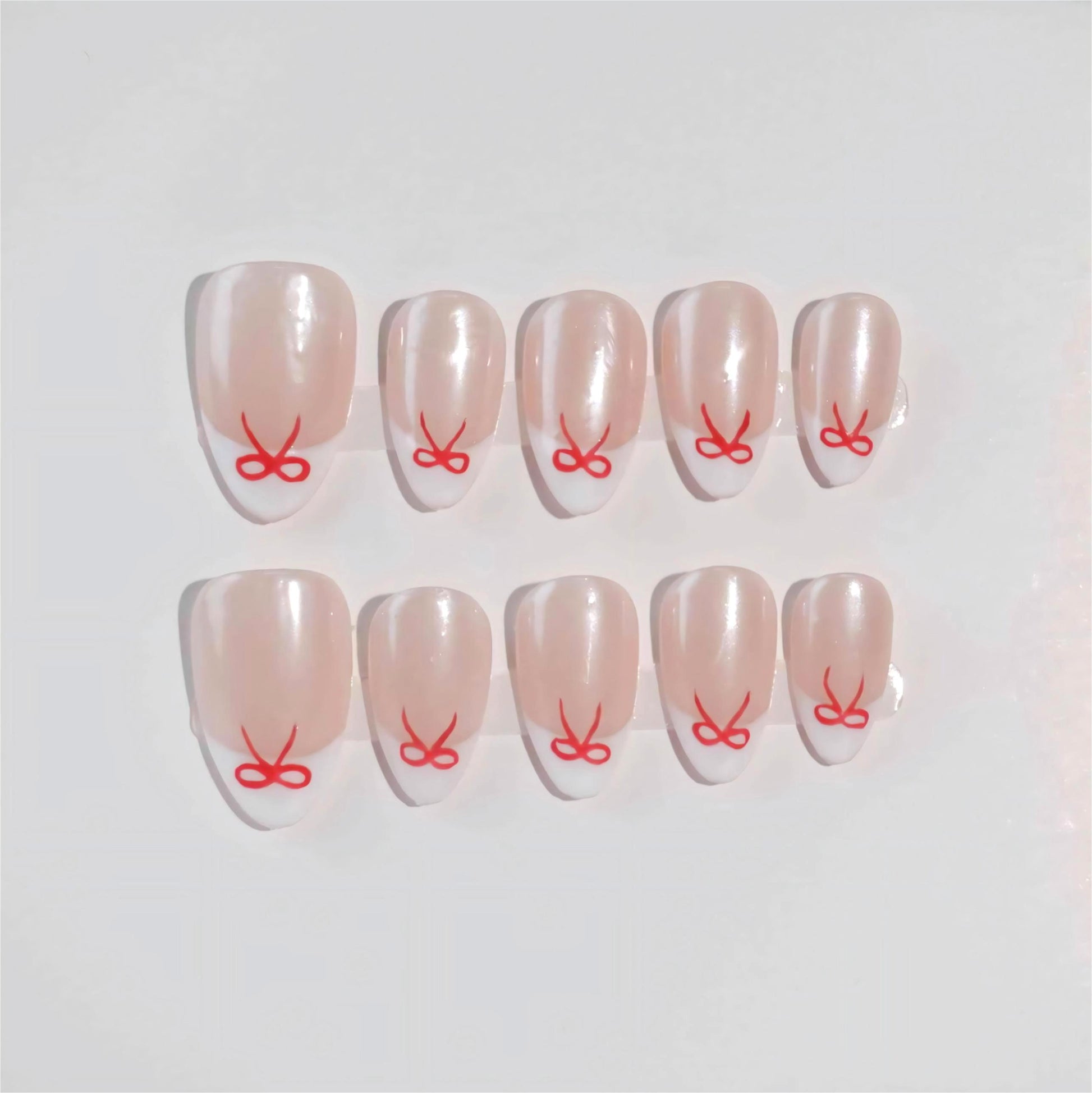 Minimalistic press-on nails featuring a nude base, white French tips, and red ribbon-inspired designs for a stylish and sophisticated look.