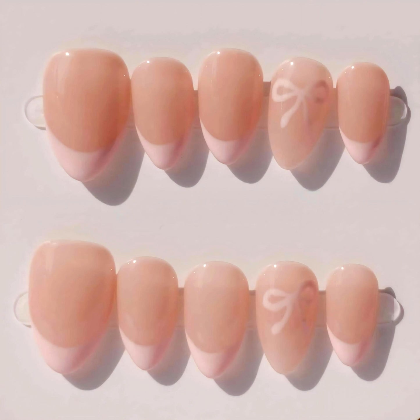 Soft pink French nails with 3D bowknot decorations, presenting a delicate and adorable aesthetic.