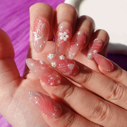 A charming set of handmade press-on nails adorned with intricate pink flowers, glittering details, and ethereal designs, radiating a soft, romantic glow.