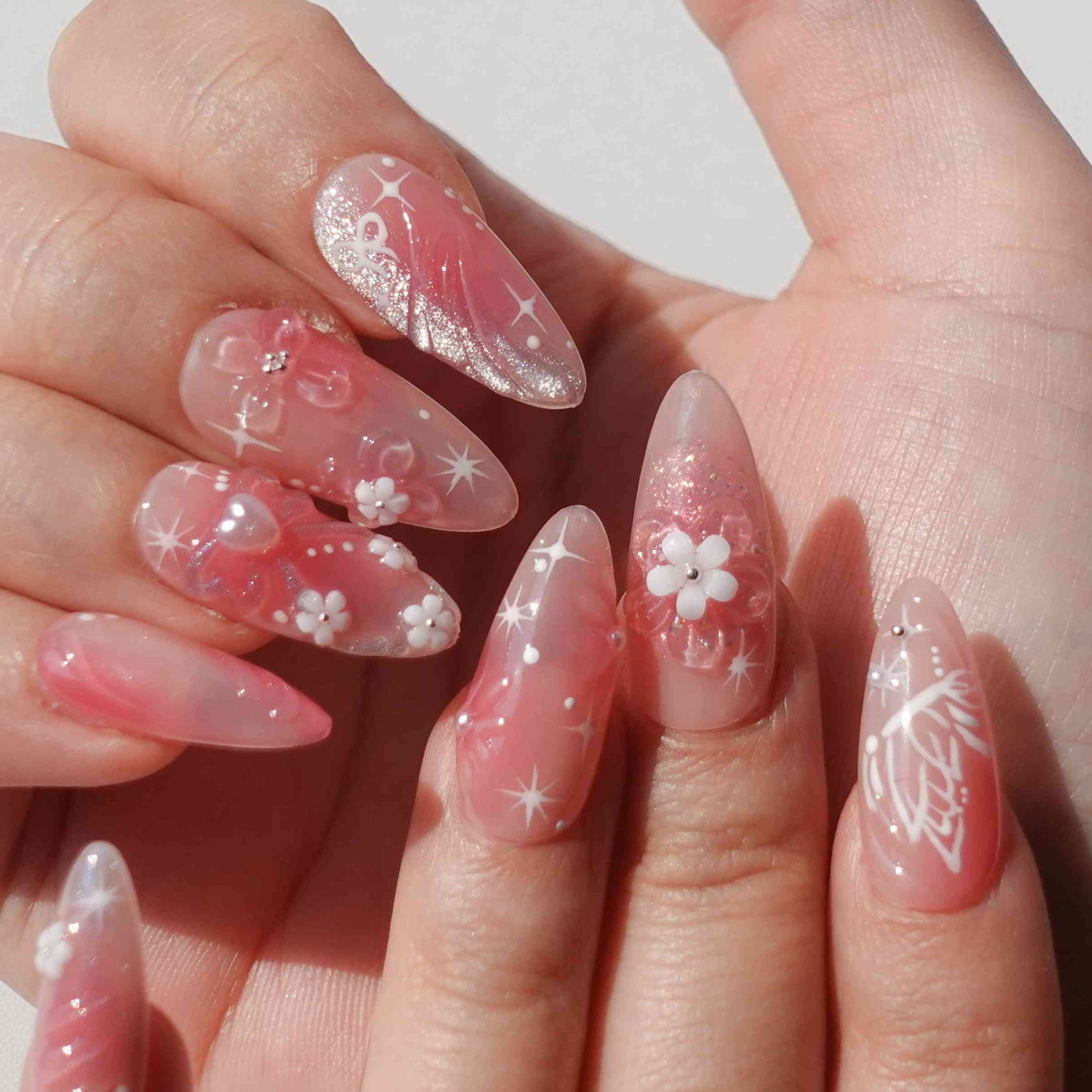 A charming set of handmade press-on nails adorned with intricate pink flowers, glittering details, and ethereal designs, radiating a soft, romantic glow.