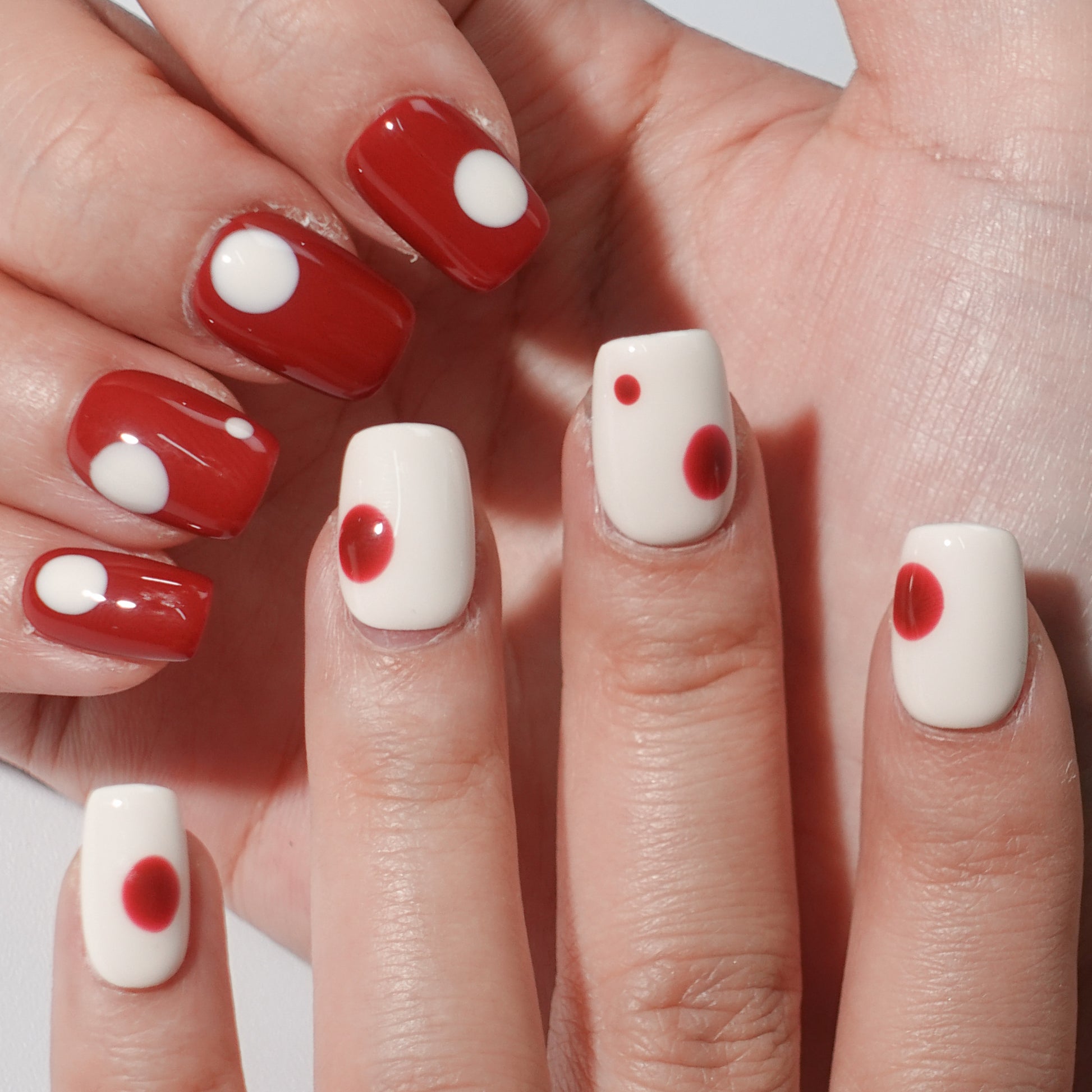 A set of press - on nails with a classic contrast of white and red, worn on a person's hand. The nails have a smooth finish with circular patterns, ideal for creating a bold and elegant appearance, suitable for both casual and formal events.